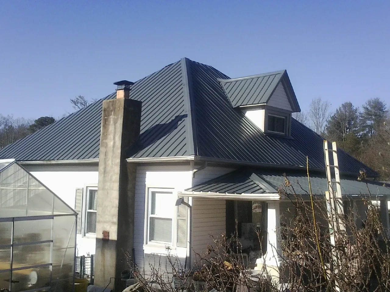 Dark blue standing seam metal roof on a white farmhouse with dormer — Slate & Tile Roof Repair by Roofing Brothers in Prosper