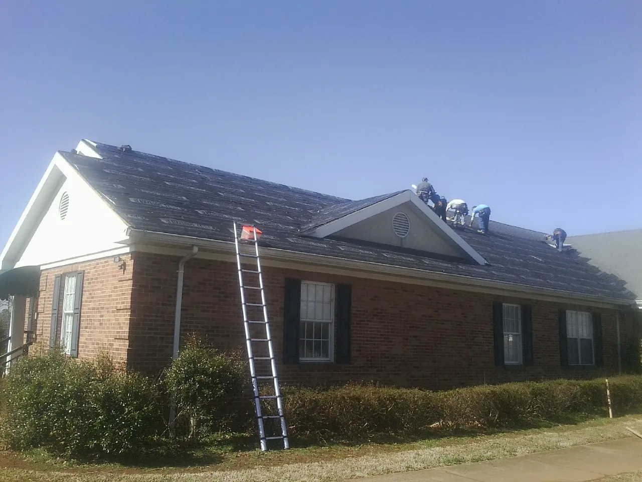 Crew tearing shingles off a brick ranch roof with a ladder set — Metal Roof Repair work by our crew in Prosper