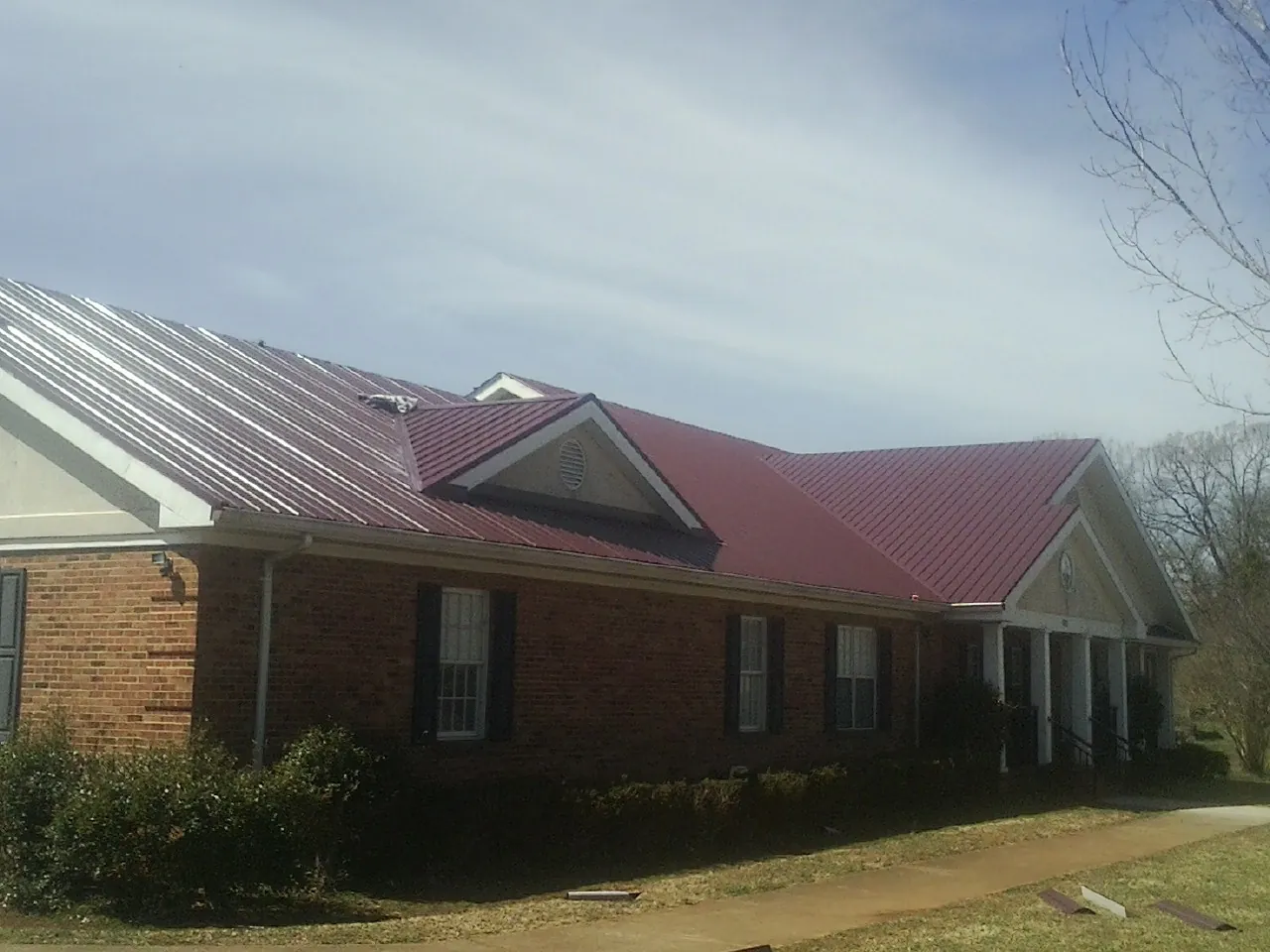 Red metal roof with gabled entries on a long brick building, from a Hail Damage Roof Repair job in Prosper