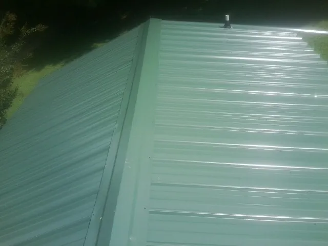 New green metal panels meeting at the ridge of a roof — Flat Roof Repair work by our crew in Prosper