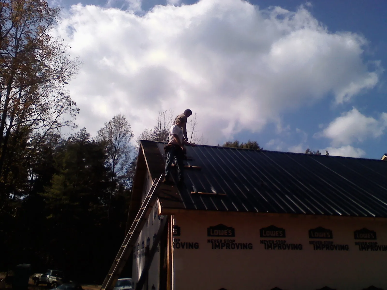 Roofer fastening dark metal panels high against a cloudy sky, from a Roof Inspection job in Prosper