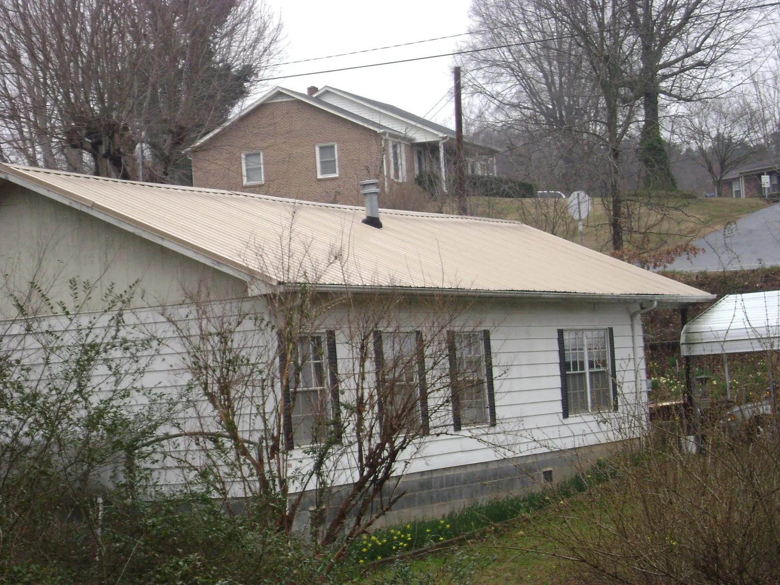 Tan metal roof on a white sided house set into a hillside — Commercial Roofing by Roofing Brothers in Prosper